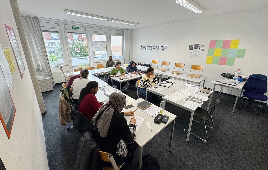 Unterrichtsraum im IB Sprachinstitut Böblingen, Schüler*innen sitzen an Tischen und lernen, an den Wänden sind Plakate zu sehen. Der Raum ist hell beleuchtet.