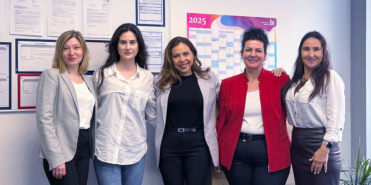 Das Team des IB Sprachinstitut Böblingen steht vor einer weißen Wand mit Kalendern und diversen anderen Informationen und schaut in die Kamera.